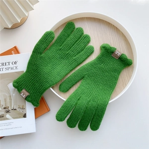 Detail of bright green knitted gloves with decorative leather patch on wooden tray