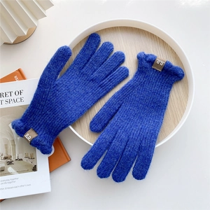 Detailed close-up of blue knitted gloves with leather logo patch on a wooden tray