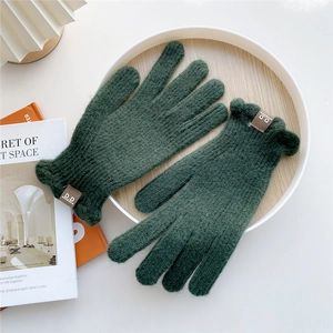 Detail of dark green knit gloves featuring scalloped cuffs and a brown leather logo patch