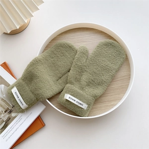 Close-up of green knitted mittens with HAND MADE label on a white wooden tray