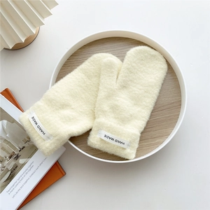 Close-up of beige thick knit mittens with a stitched Hand Made label on the cuff