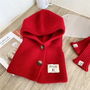 Detail of red knit hood scarf with wood buttons and matching gloves on a wooden desk