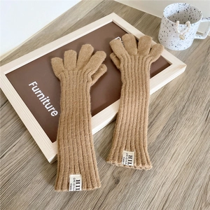 Detail of camel knitted long gloves featuring ribbed texture and stylish fabric label