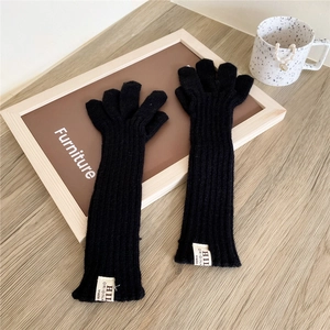 Long black ribbed knit gloves with white logo label on a rustic wooden table background