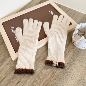 Detail of cream knit gloves with brown ribbed cuffs and woven label on a wooden table