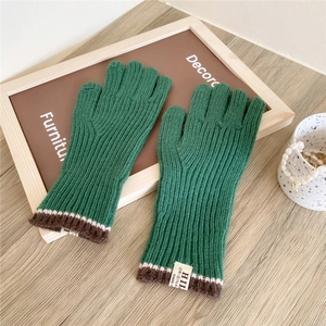 Detail of green knit gloves with ribbed texture and striped cuff on wooden background