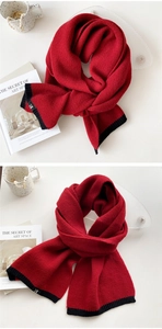 Detail of red knitted scarf with black ribbed edges and small letter H label tag