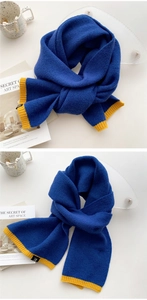 Detail of navy knit scarf with yellow contrast edge and premium brand label on white desk