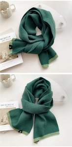 Detail of dark green knitted scarf featuring soft wool texture and a black lettered tag