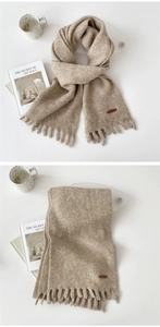 Detail of beige solid color winter scarf with fringe trim and leather brand tag label