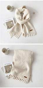 Detail of solid off-white knit scarf with fringe and vintage brown faux leather label