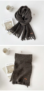 Detail of dark grey knit scarf with tassels and small brown leather label tag