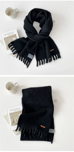 Detail of thick black knitted winter scarf with fringe trim and leather brand patch