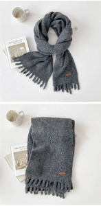 Close-up of thick dark grey tassel scarf with soft knit texture and leather label