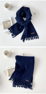 Detail of navy blue knitted scarf showing thick texture, fringe, and brown leather label