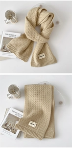 Detail of oatmeal knit scarf showing honeycomb texture and brand label on a white surface