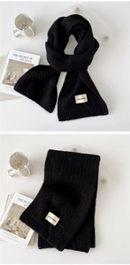 Detail of black thick knit scarf with woven fabric label and soft warm texture