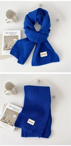 Detail of royal blue thick knit scarf with square brand label on minimalist background