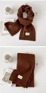 Detailed close-up of dark brown knit scarf featuring hollow crochet texture and brand label