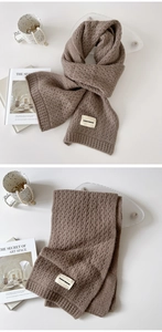 Detail of dark brown knitted scarf with wave texture and woven label in a minimalist setting