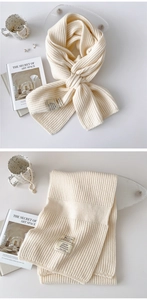 Detail of cream knitted scarf with ribbed texture, fabric care label and decorative tag