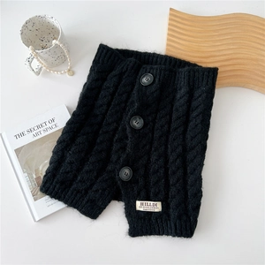 Detail of black cable-knit buttoned neck warmer with brand label on a wooden tray