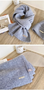 Detail of light grey 100% wool knitted scarf and hat set with metal logo plate