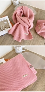 Detailed shot of pink 100% wool scarf showing ribbed knit texture and logo metal plate