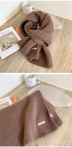 Detailed macro of brown 100% wool knitted scarf showing thick ribbed texture and metal tag