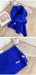 Detail of royal blue 100% wool scarf featuring a premium metal brand tag and knit texture