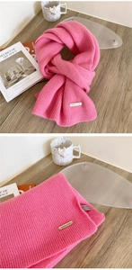 Detail of pink ribbed knit 100% wool scarf featuring refined metal brand label and texture