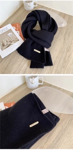 Detailed view of dark blue 100% wool scarf with vertical knit texture and metal logo tag