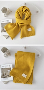 Detailed view of ginger yellow knitted scarf with soft vertical texture and woven emo label
