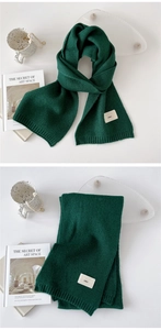 Detail showing deep green knitted scarf texture with minimalist logo label and soft finish