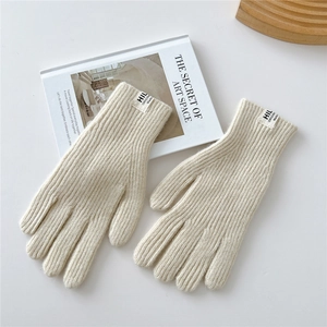 Detailed close-up of cream knit gloves with ribbed texture on a wooden tray