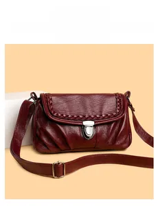 Détail d'un sac bandoulière bordeaux en cuir froissé avec bord tressé et boucle argentée