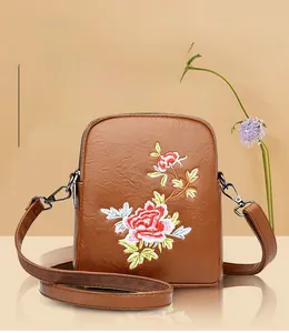 Detailed close-up of colorful floral embroidery and metal lobster clasp on the brown bag