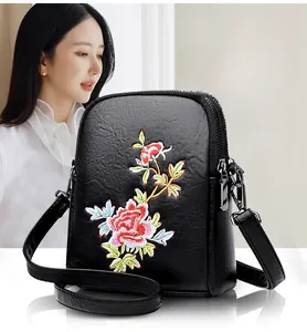 Detail of red and yellow floral embroidery on black faux leather crossbody phone bag
