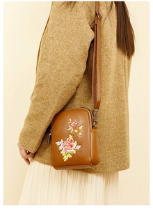 Detail of red floral embroidery on a brown PU leather crossbody bag with a zipper