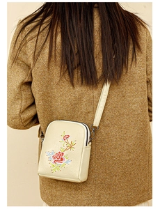 Detail of embroidered floral crossbody phone bag worn over a textured brown tweed coat