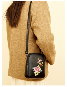 Detail of floral embroidery on a black faux leather crossbody mobile phone bag with strap