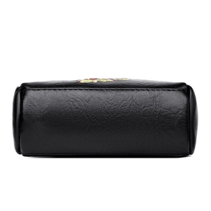 Bottom view of black leather phone bag featuring floral embroidery and grain texture