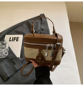 Detail of color-block box bag featuring brown leather and beige canvas with dual zippers