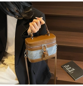 Detail view of cylinder bag with brown leather and blue denim stitching and chain