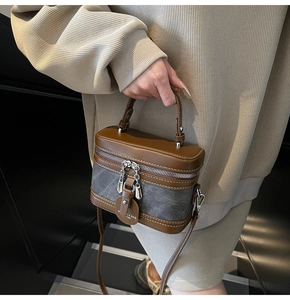 Détail du sac boîte cylindrique en cuir marron et toile grise avec boucles argentées