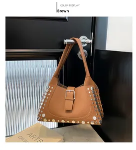 Dettaglio borsa a secchiello in pelle marrone con borchie appesa a una porta di legno