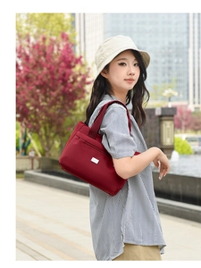 Dettaglio della borsa a spalla in nylon bordeaux con tasca a zip e placca logo in metallo
