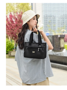 Dettaglio della borsa tote in nylon nero con tasca frontale a zip e logo in metallo