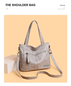 Detail of gray faux leather tote bag showing the front zipper pocket and metal logo plaque