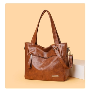 Detail view of caramel brown tote bag with metal logo, zipper pocket and strap